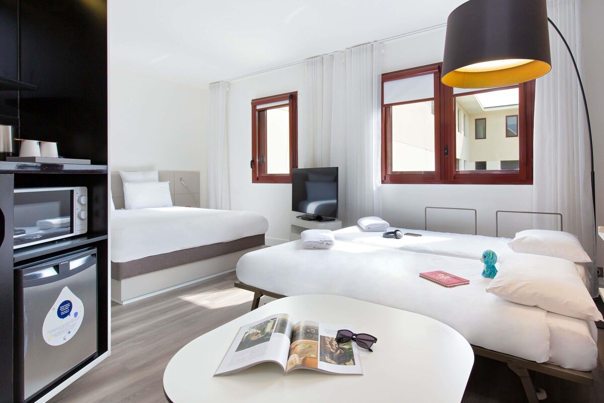 A hotel room with a bed, a desk, a TV, a lamp, and a microwave.