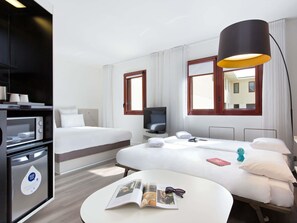 Une chambre d’hôtel équipée d’un lit, d’un bureau, d’une télévision, d’une lampe et d’un four à micro-ondes.