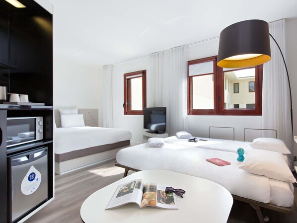 A hotel room with a bed, a desk, a TV, a lamp, and a microwave.