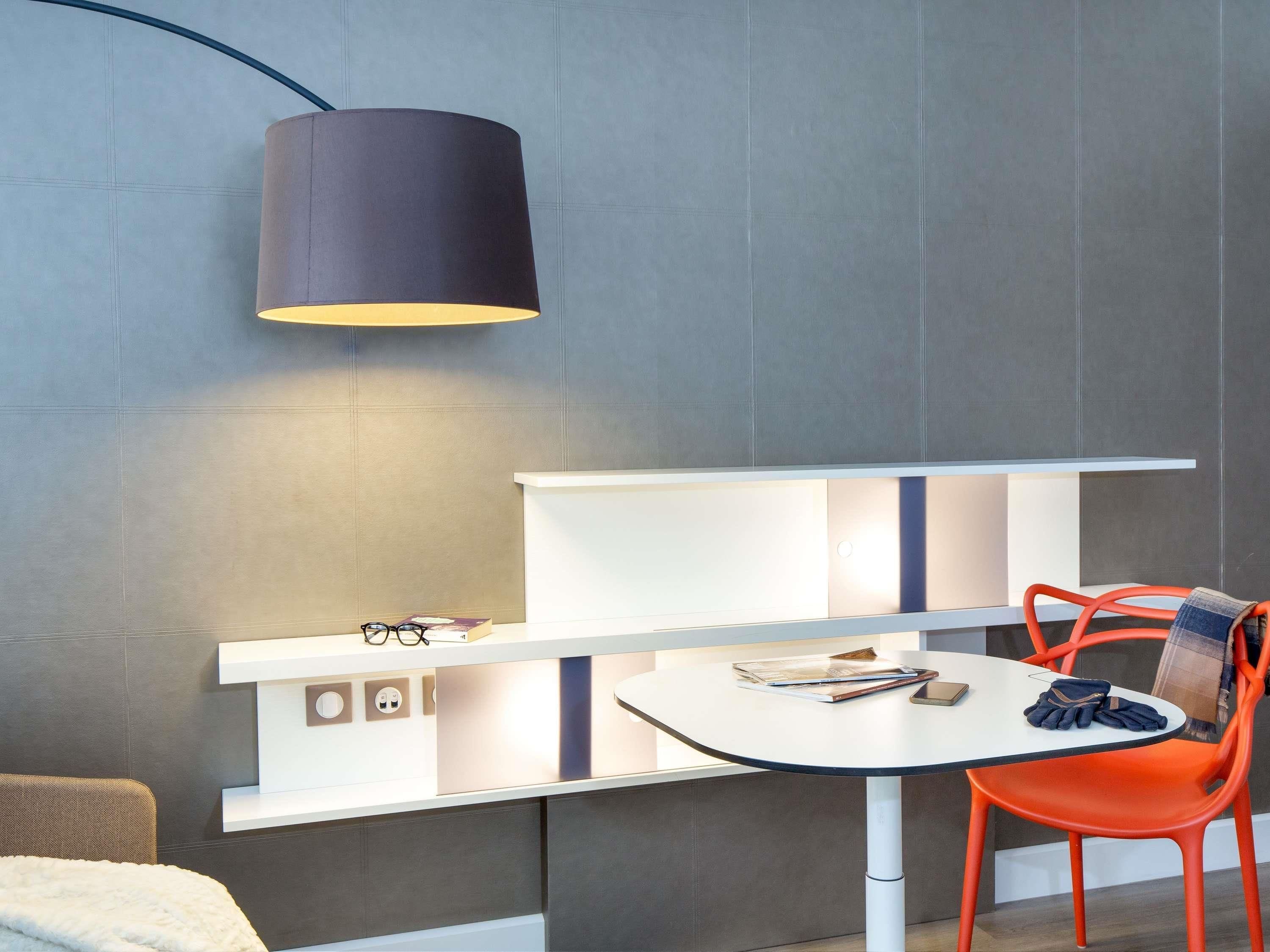 A modern room with a white table, orange chairs, a black lamp, and a white shelf with a magazine and glasses.