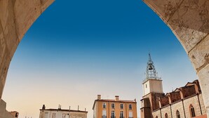 Una estructura de piedra con arco enmarca la vista de un edificio con una torre y una campana.