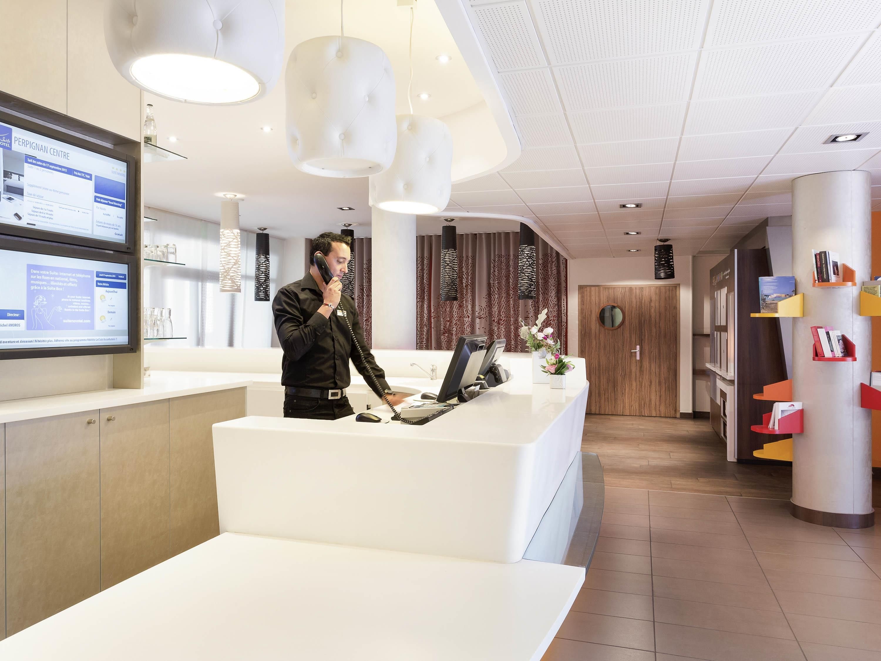 Ein moderner Hotel-Empfangsbereich mit Rezeptionist, Computer und digitalem Bildschirm.