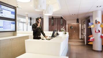 Una moderna zona de recepción de hotel con una recepcionista, una computadora y una pantalla digital.