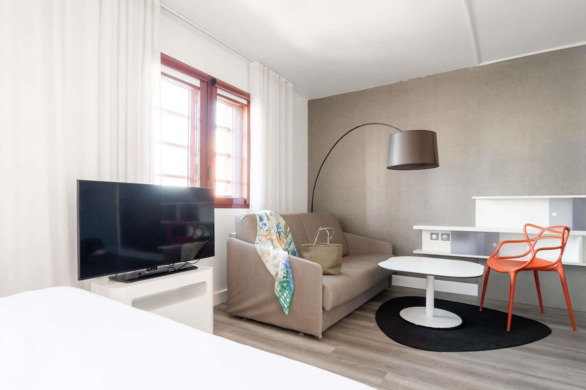 Una habitación de hotel moderna con televisor de pantalla plana, un sofá, una pequeña mesa de comedor y una silla.