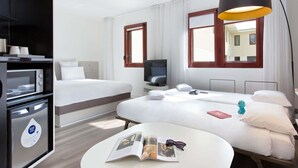 A hotel room with a bed, a desk, a TV, a lamp, and a microwave. - Novotel Suites Perpignan Mediterranée (Perpignan)