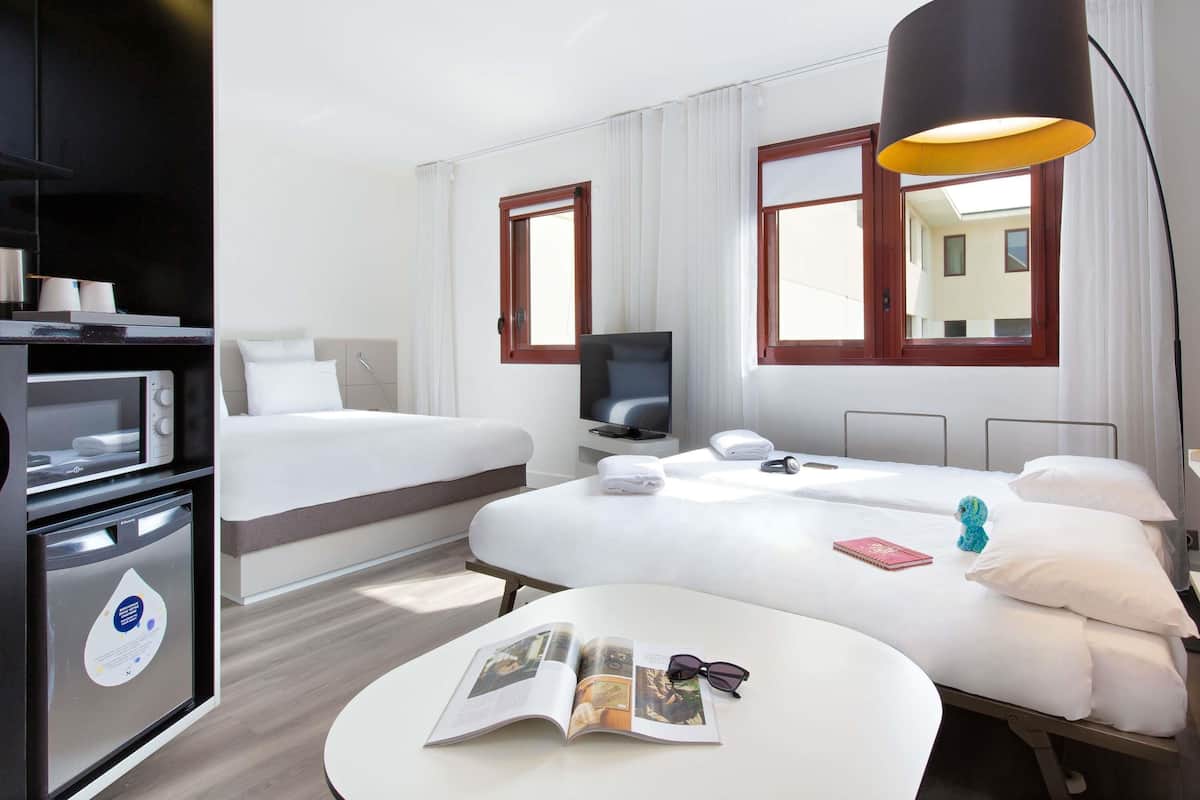 A hotel room with a bed, a desk, a TV, a lamp, and a microwave.