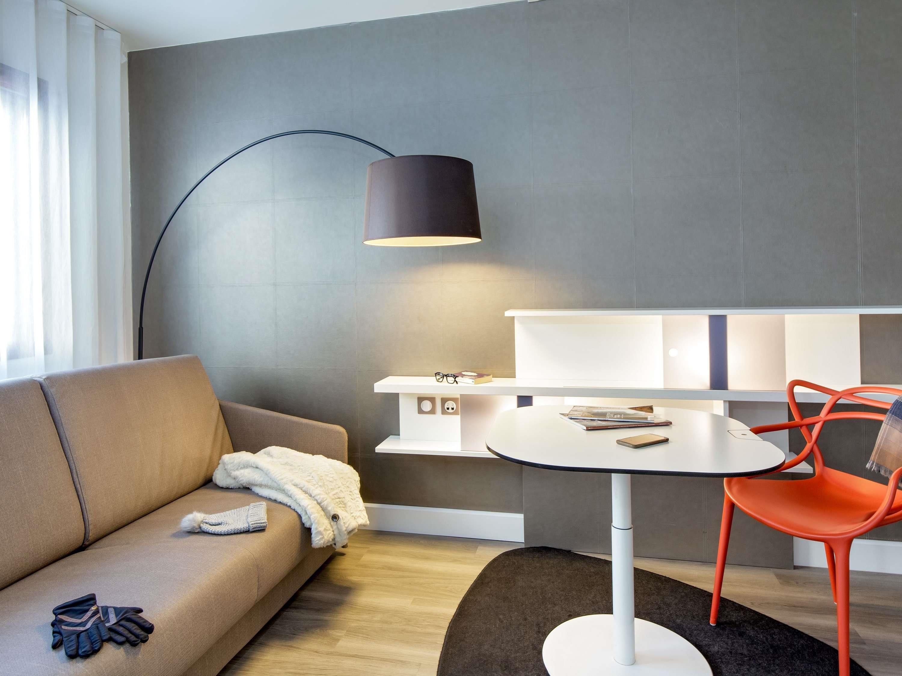 Ein modernes Wohnzimmer mit einer Couch, einem Couchtisch, einem roten Sessel, einer Stehlampe und einem Bücherregal.
