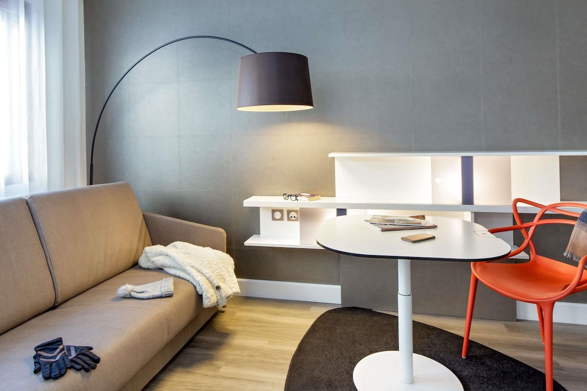 A modern living room with a sofa, a coffee table, a red chair, a floor lamp, and a bookshelf.