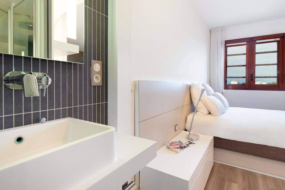 A modern bathroom with a white sink, a mirror, and a wall-mounted outlet.