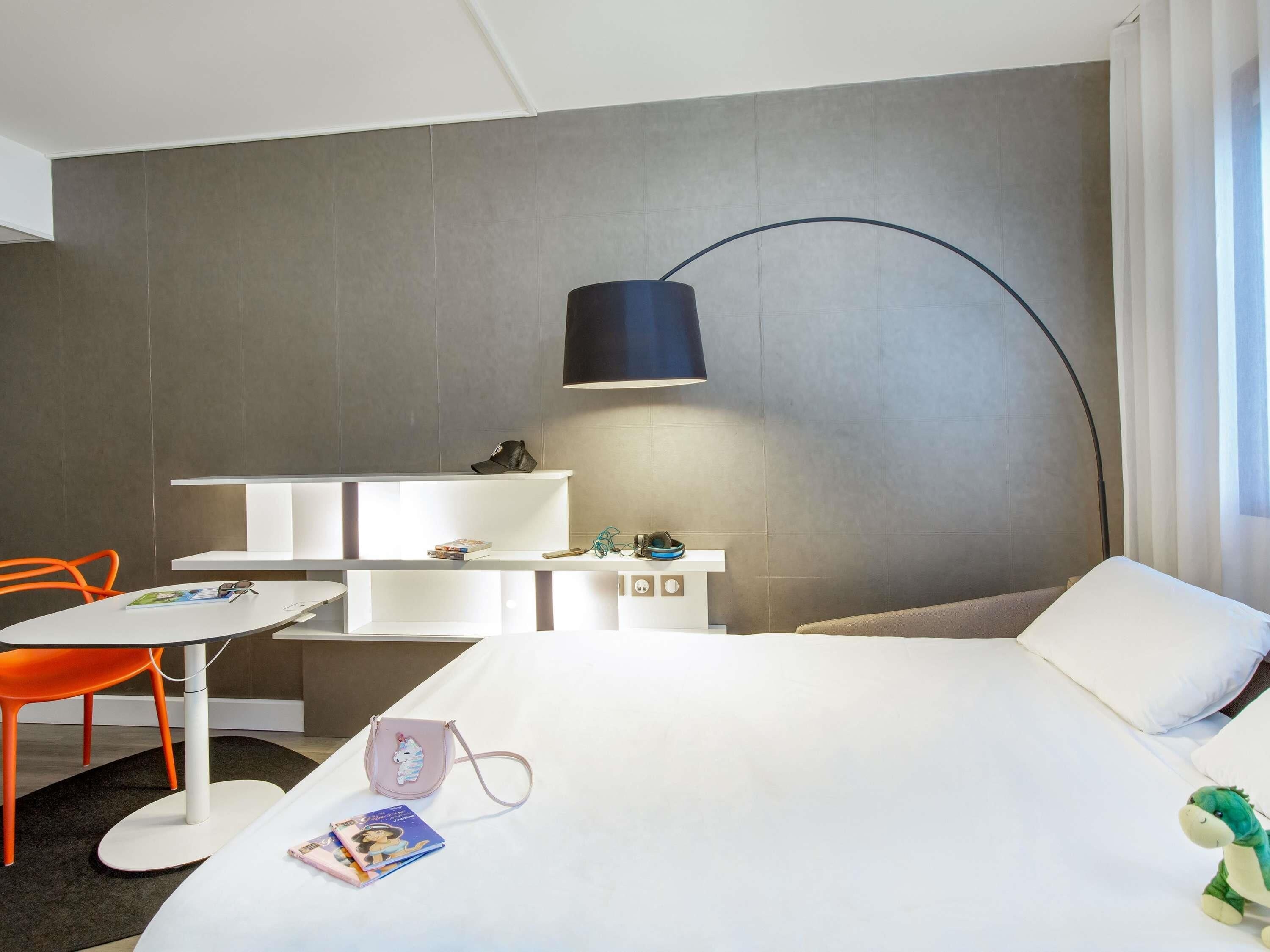 Une chambre d’hôtel moderne équipée d’un lit, d’un bureau, d’une chaise et d’une lampe.
