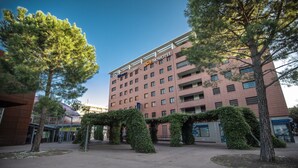 A hotel with a red facade, multiple floors, and a central courtyard with trees and shrubs.