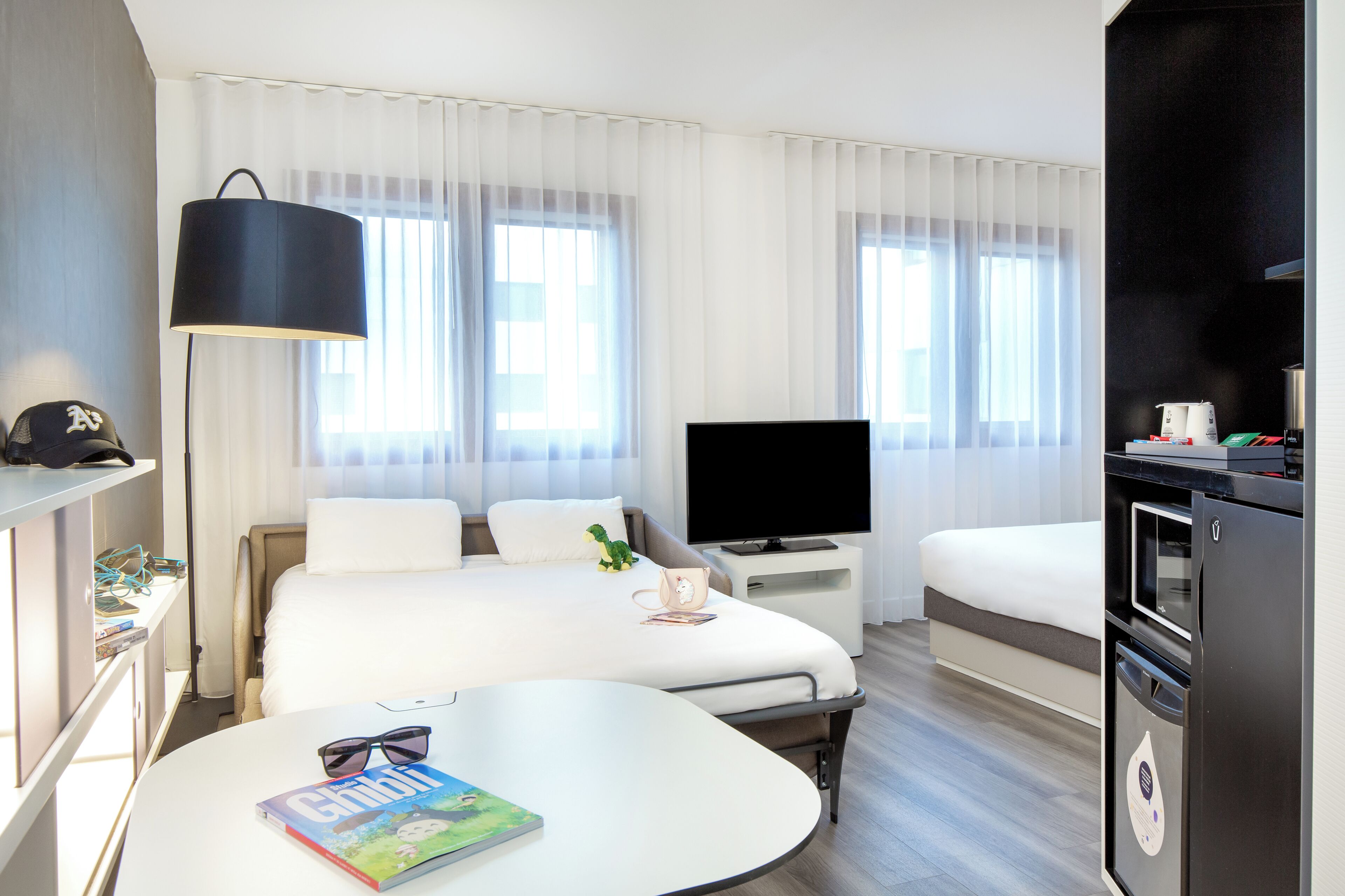Habitación de hotel con cama, televisor, escritorio, silla, mesa y refrigerador.