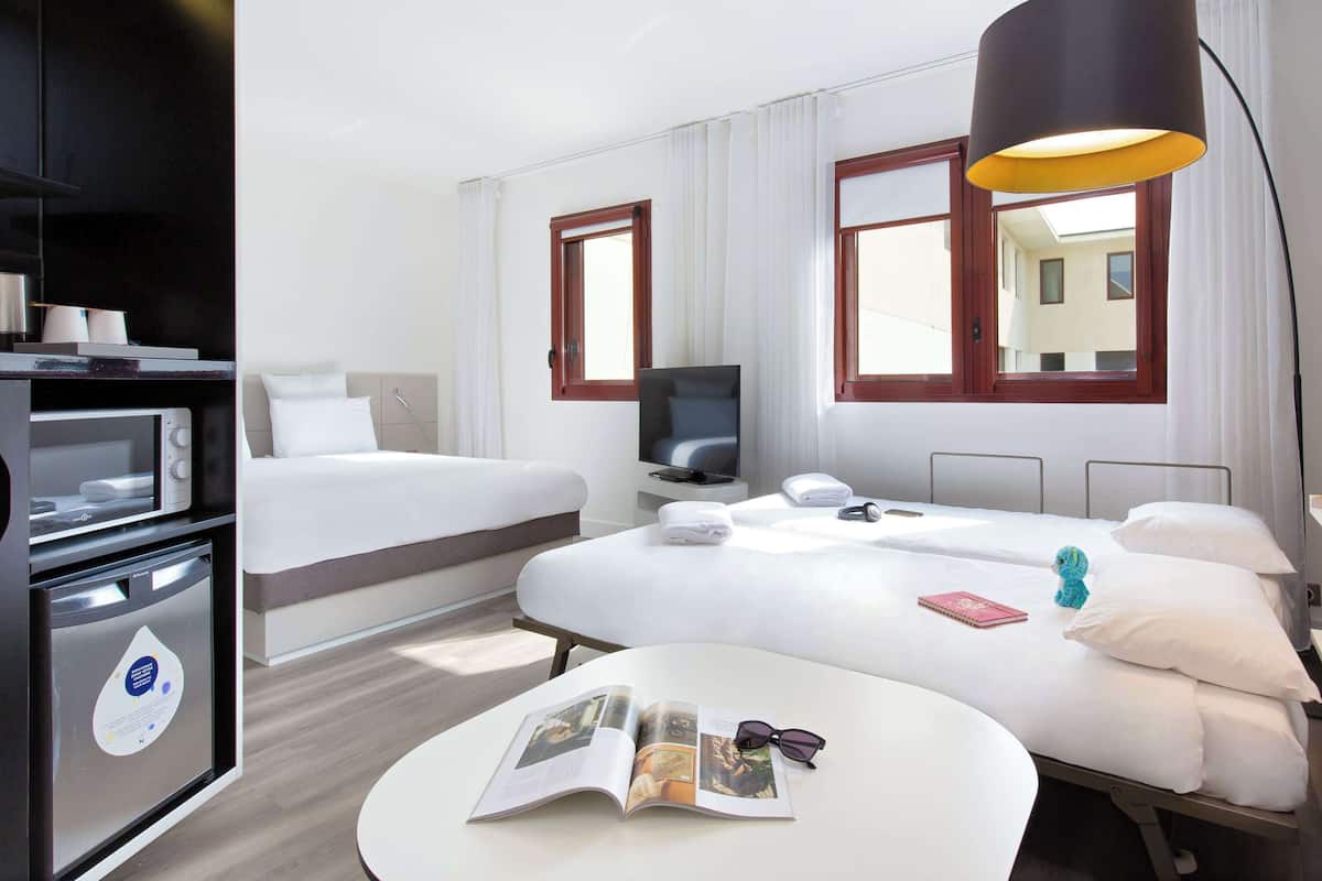 A hotel room with a bed, a desk, a TV, a lamp, and a microwave.