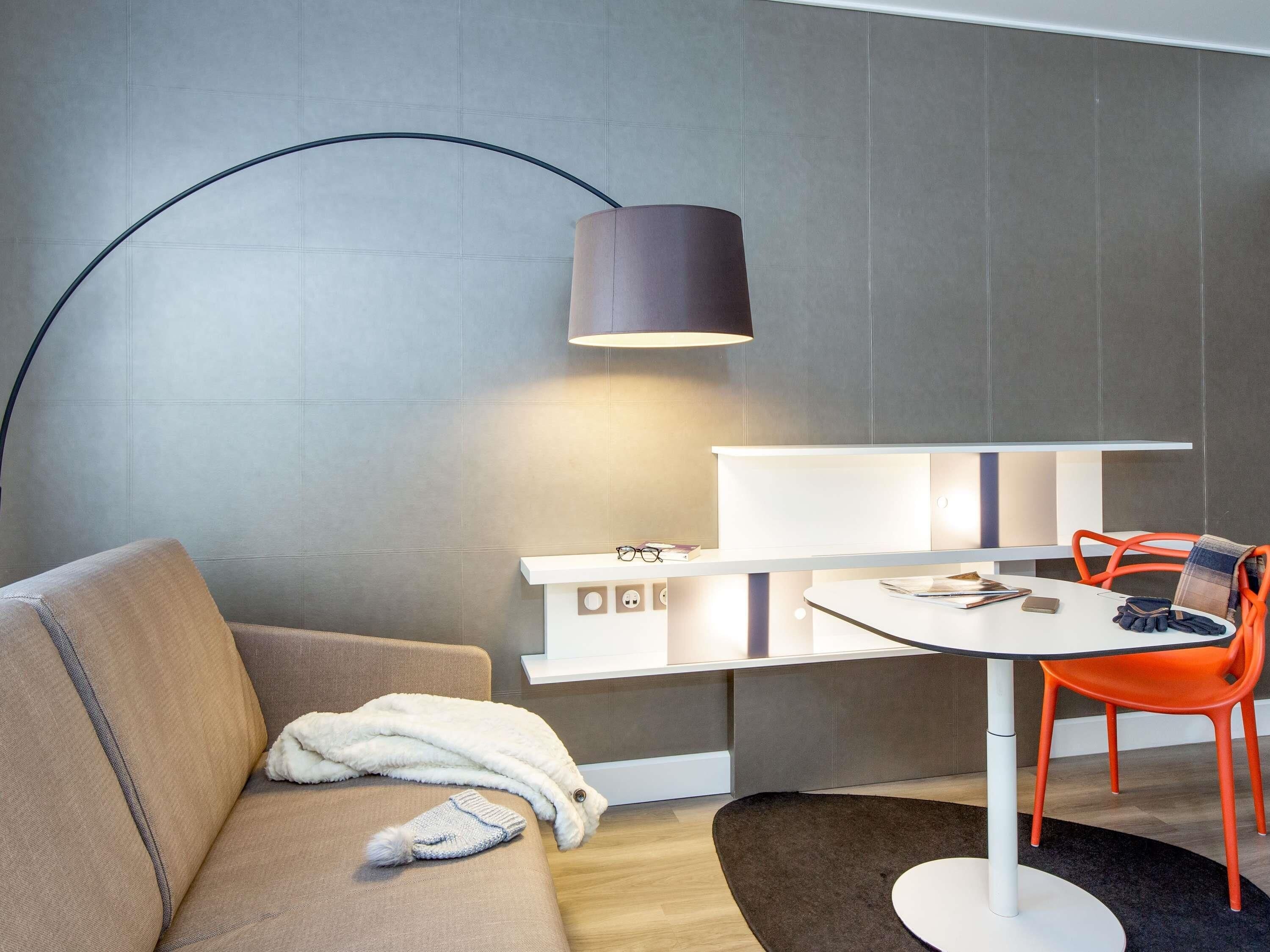 A modern room with a sofa, a table with chairs, a lamp, and a wall-mounted shelf.