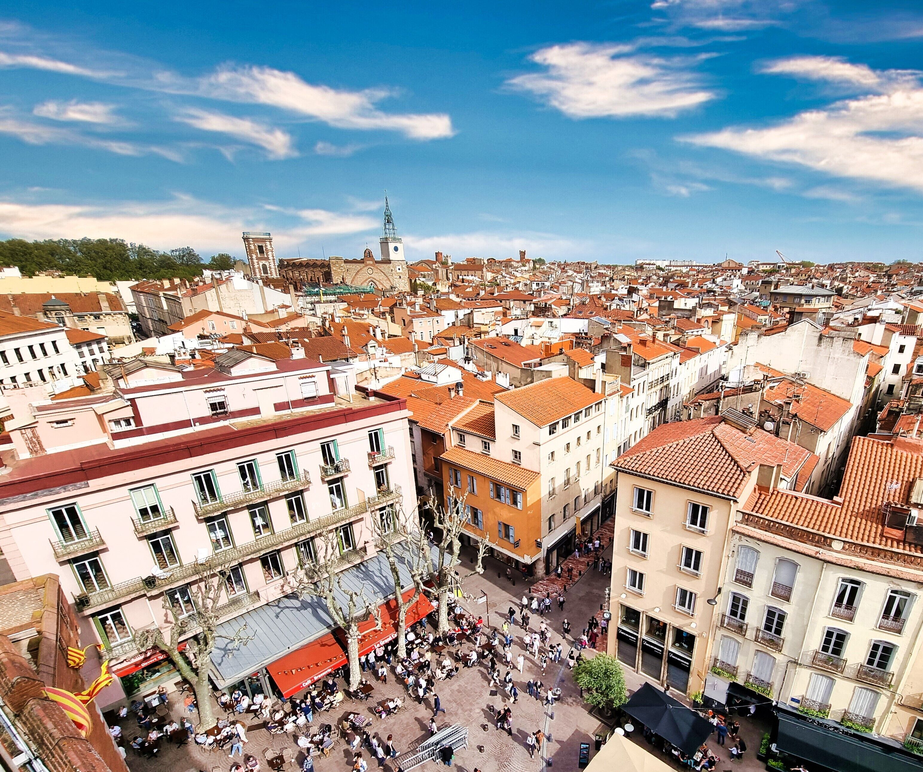 A bustling urban square with historic buildings, a prominent tower, and a clear blue sky.