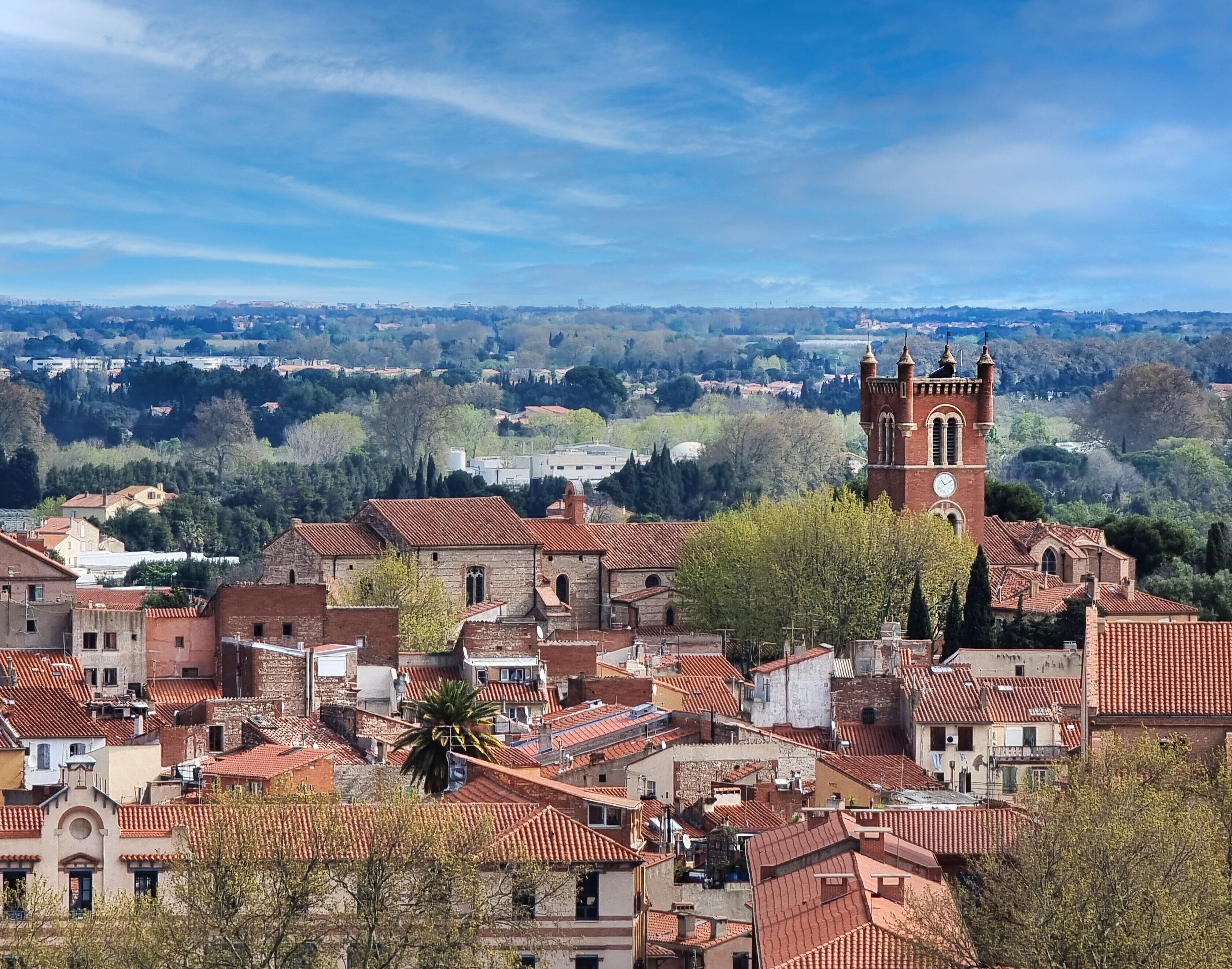 Un pueblo histórico con tejados rojos, una destacada torre de iglesia y una mezcla de edificios residenciales y comerciales.