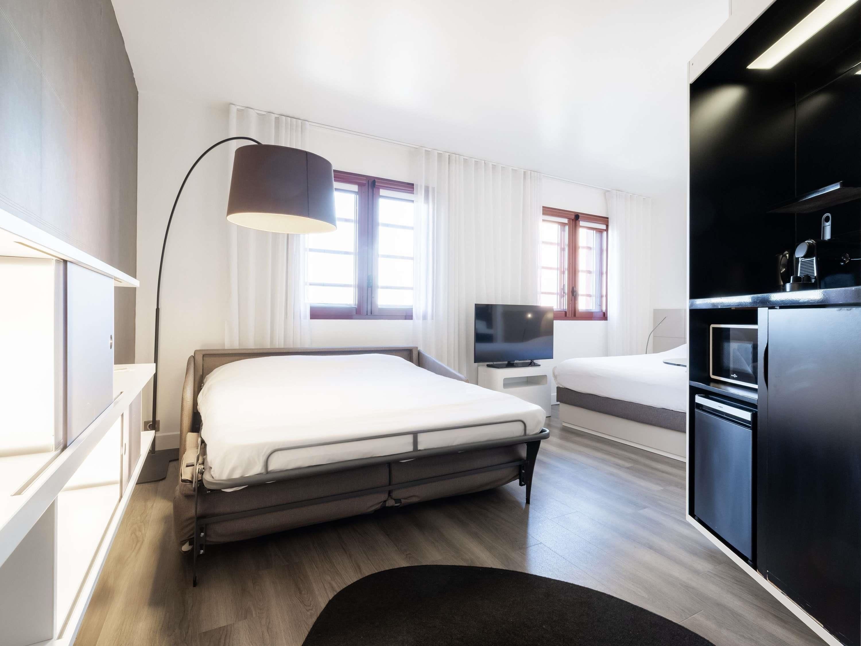 Une chambre d’hôtel moderne équipée d’un lit, d’une table de chevet, d’une télévision et d’une kitchenette.