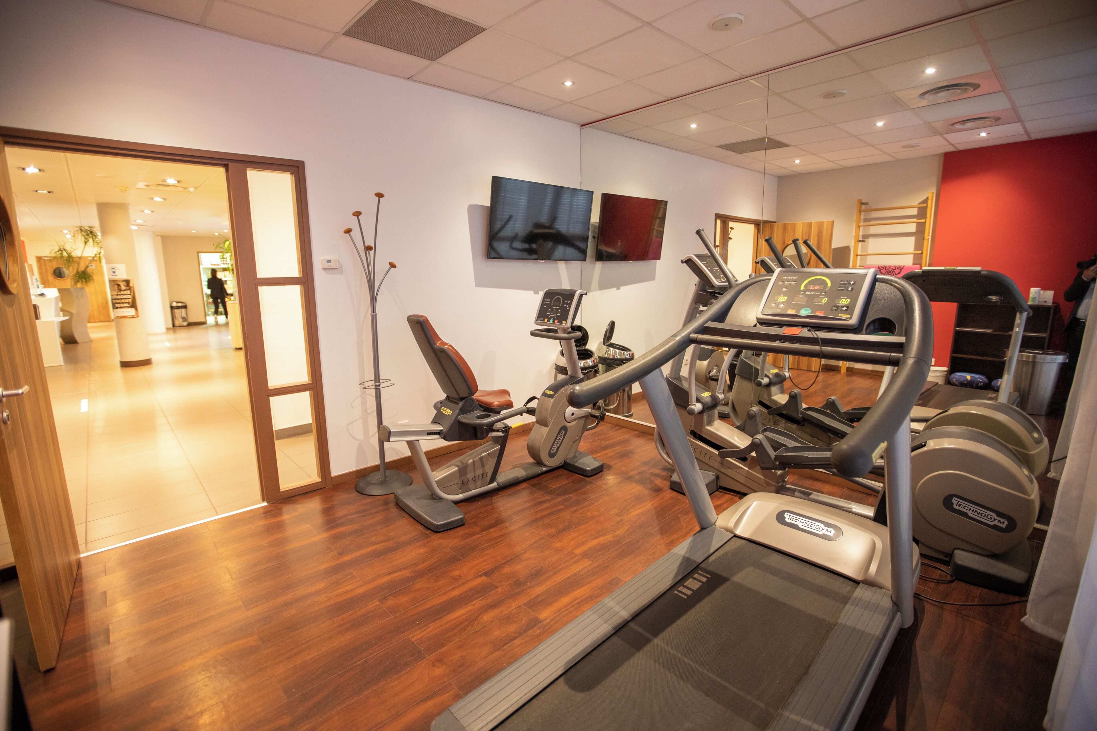 Un gimnasio con equipo de ejercicio, piso de madera y pared roja.