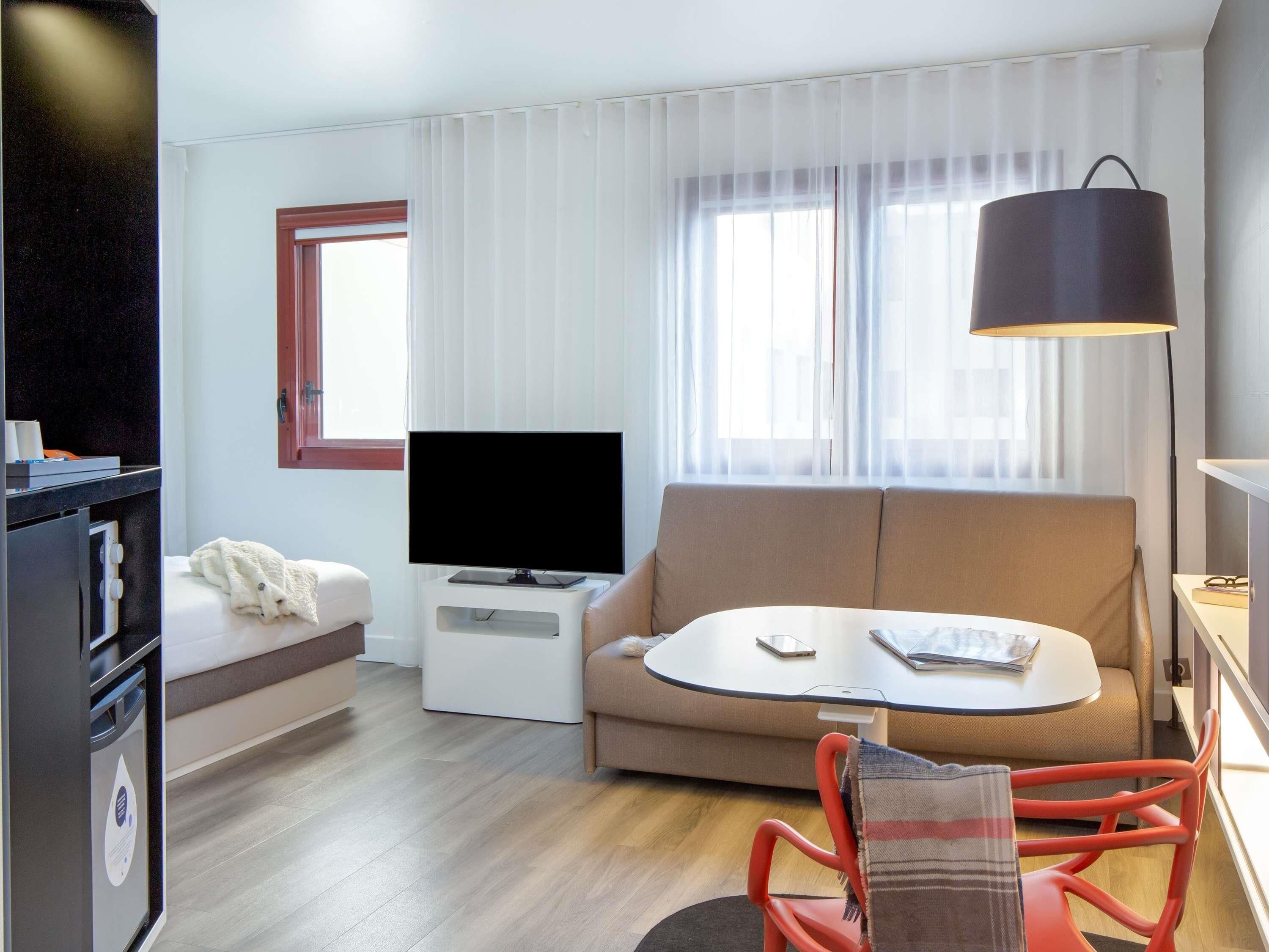 A hotel room with a sofa, a small table, a TV, a lamp, and a bed.