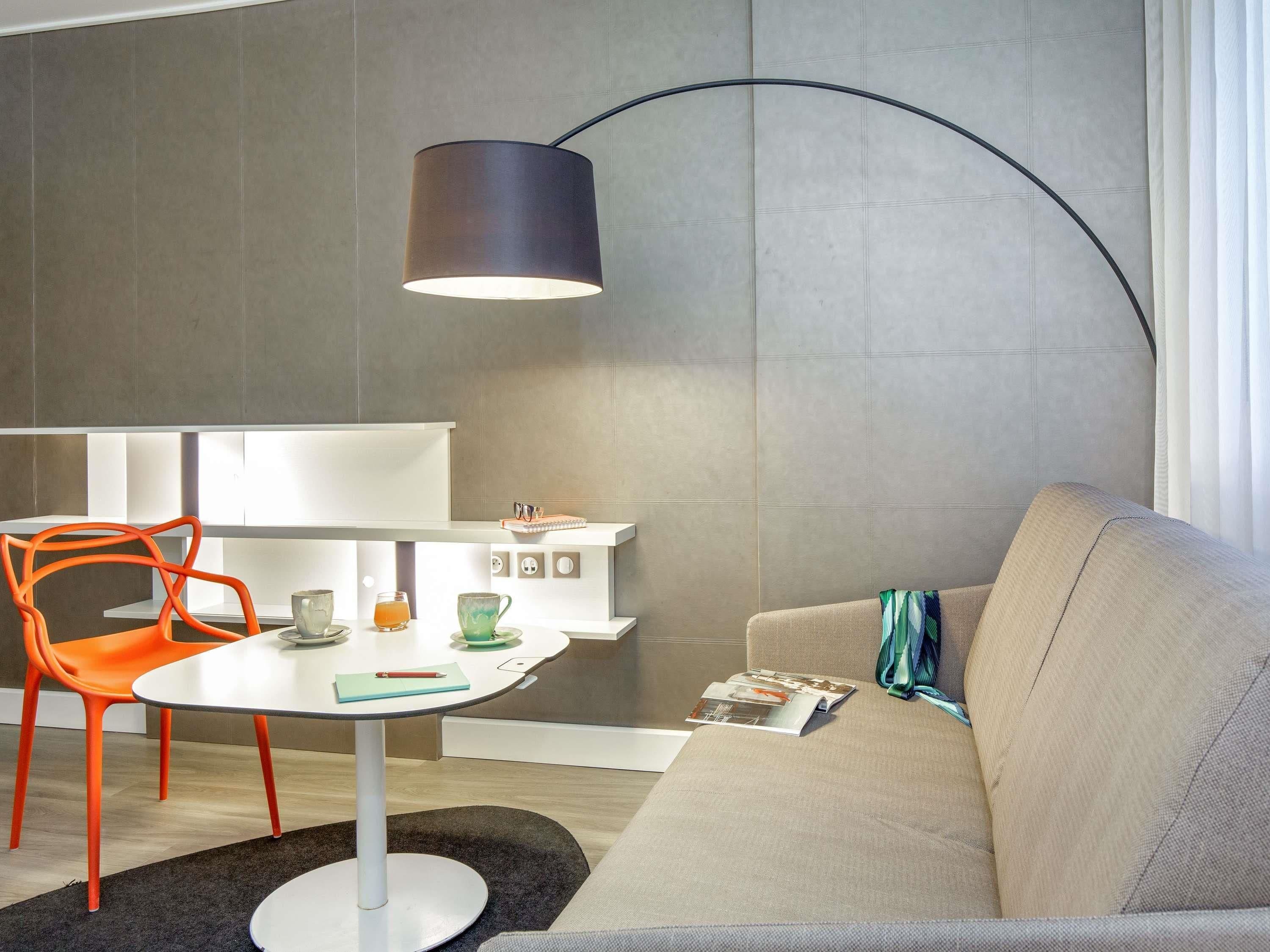 A modern living room with a round table, orange chairs, a sofa, and a floor lamp.