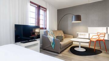 Habitación de hotel moderna con televisión de pantalla plana, sofá, una mesita, lámpara y una silla.