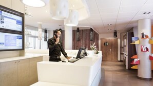 A modern hotel reception area with a receptionist, a computer, and a digital display.