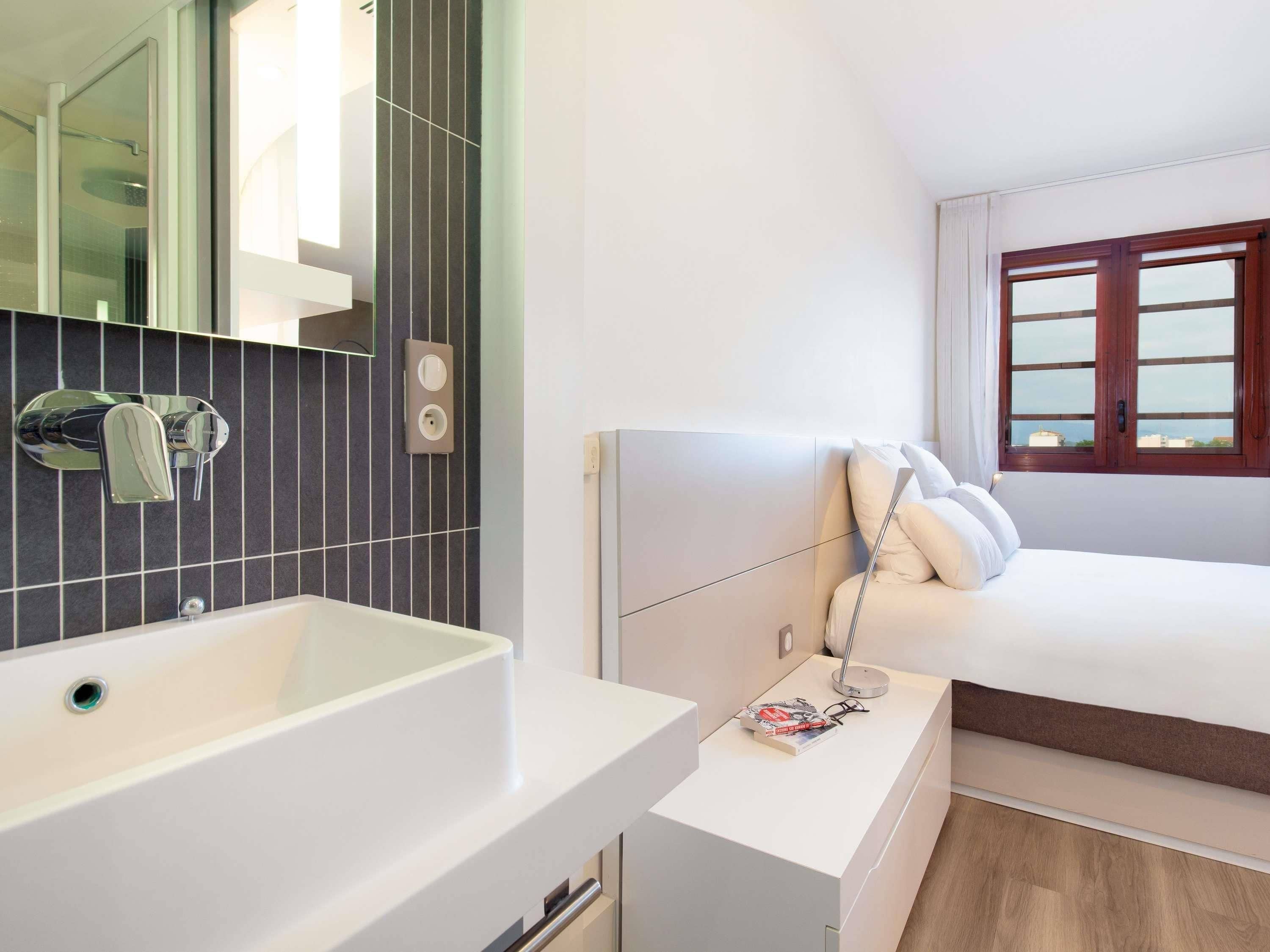 A modern bathroom with a white sink, a mirror, and a wall-mounted outlet.
