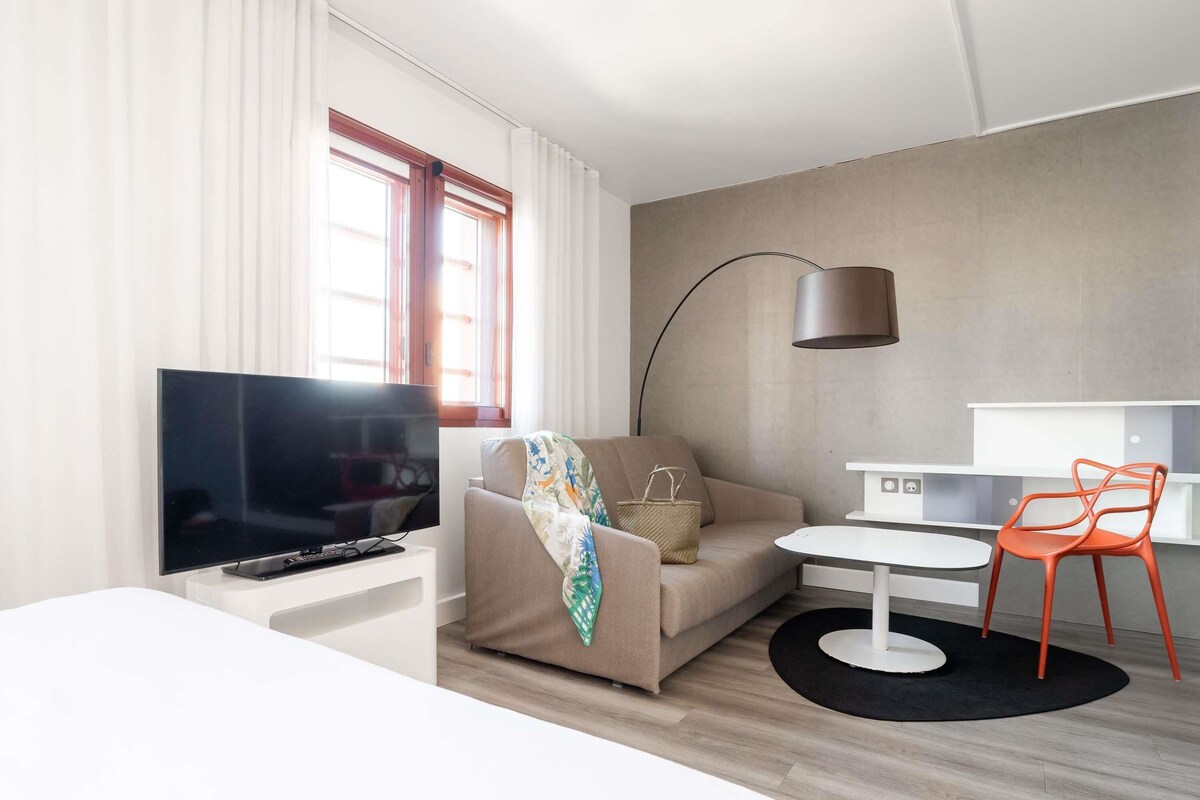 Una habitación de hotel moderna con televisor de pantalla plana, un sofá, una pequeña mesa de comedor y una silla.