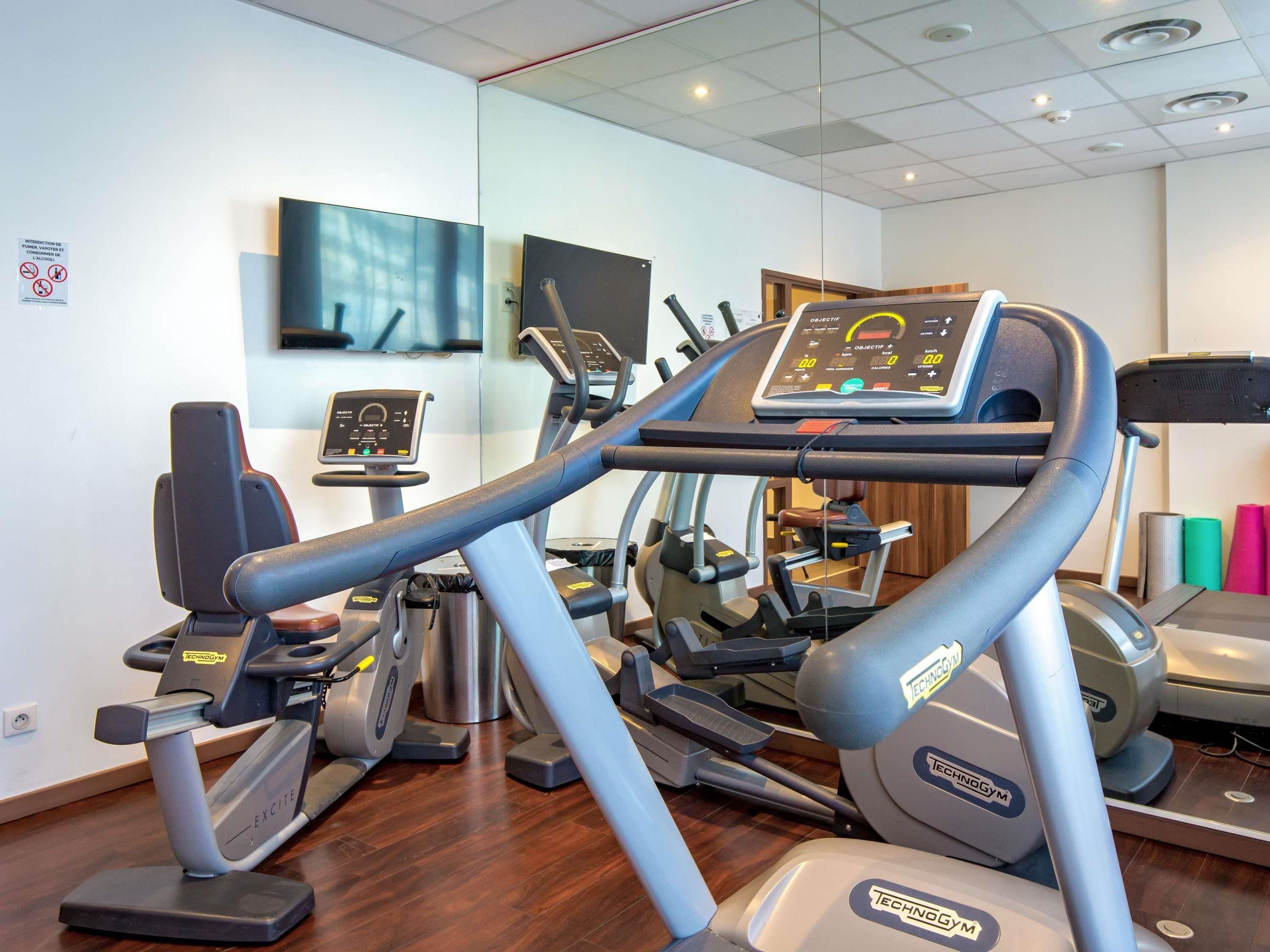 Een fitnessruimte met diverse oefenapparaten, waaronder loopbanden en elliptische trainers, en een digitaal scherm om trainingen bij te houden.