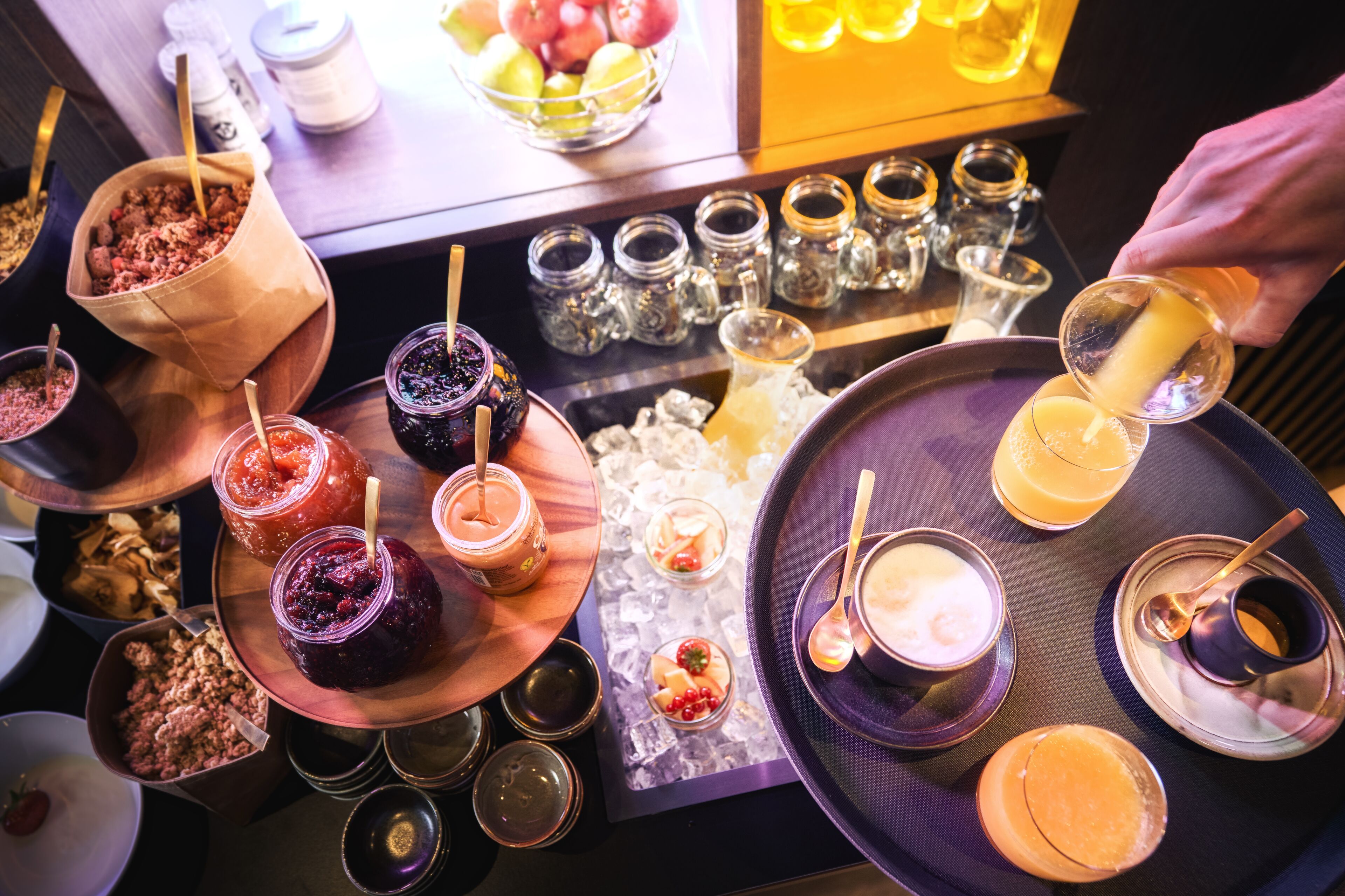 A tray with various food items and drinks, including jars of preserves, bowls of fruit, and a cup of coffee.