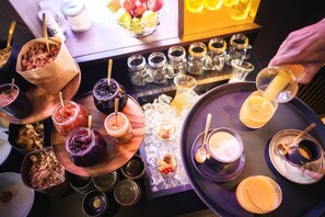 Una bandeja con diversos alimentos y bebidas, incluyendo tarros de conservas, cuencos de fruta y una taza de café.