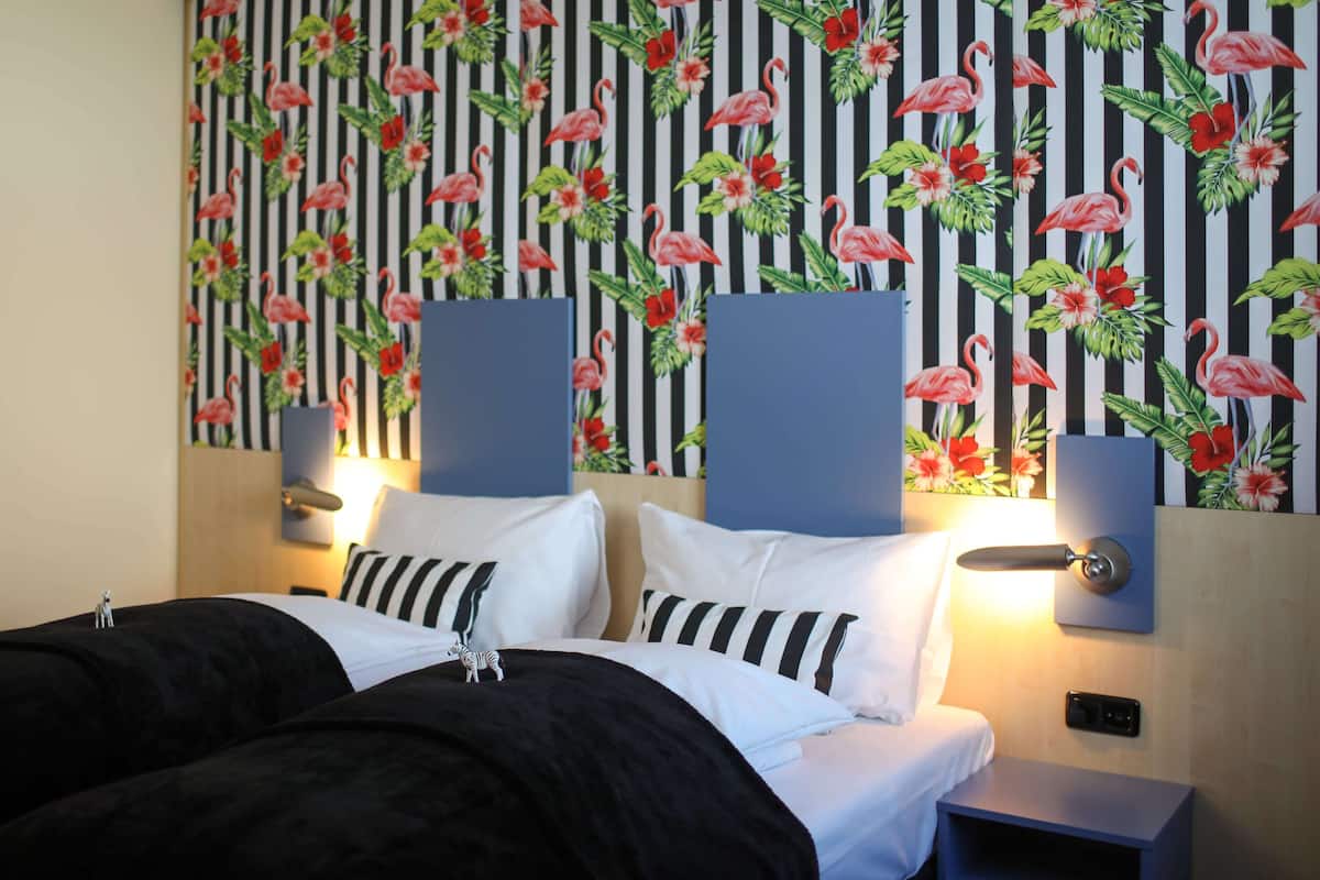 Une chambre d’hôtel avec un lit, deux tables de chevet et un mur orné d’un motif à rayures et d’un papier peint à motifs de flamants roses.