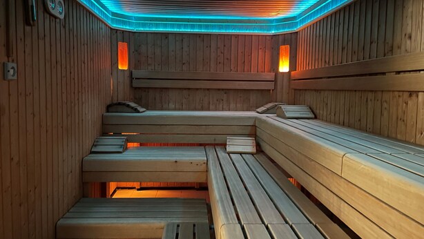 Een sauna met houten banken, verlichting in blauw en wandradiatoren.