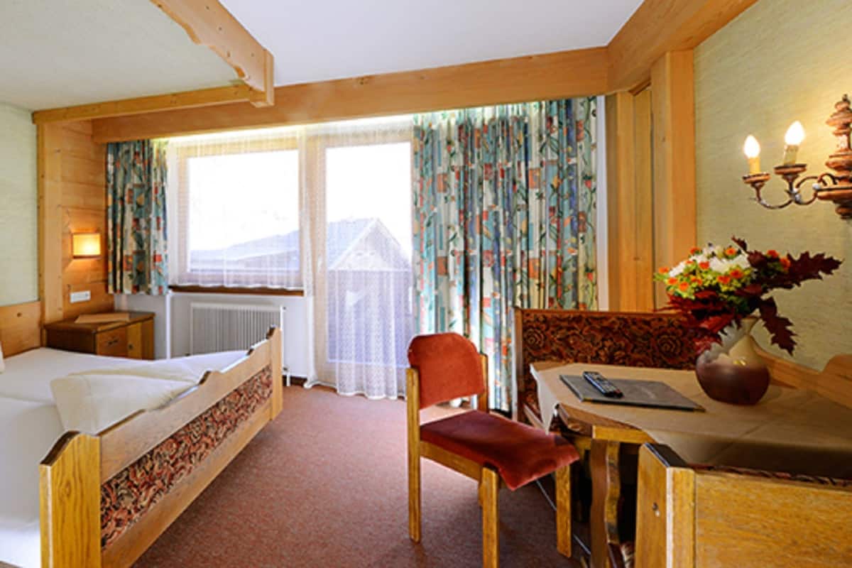 A wooden room with a bed, a chair, a table, and a vase with flowers.