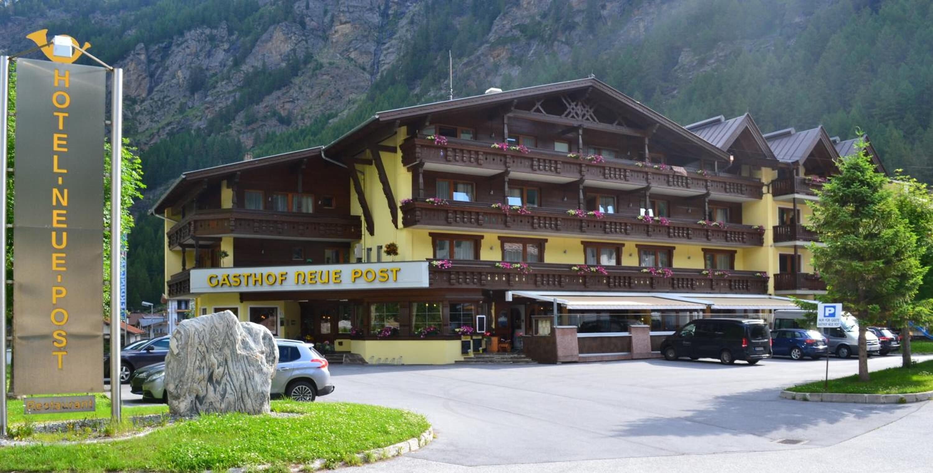 A hotel with a sign reading "HOTEL NEUE POST" and "GASTHOF NEUE POST" in front of a mountain backdrop.