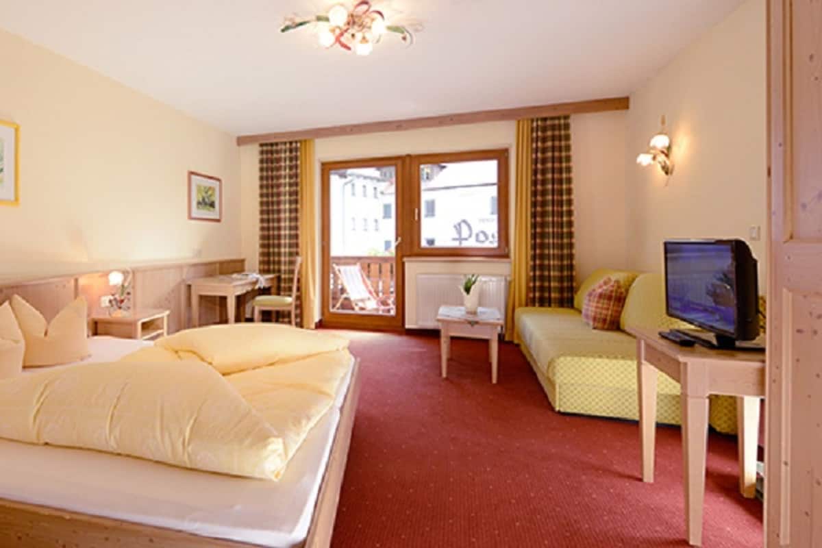 A hotel room with a large bed, a television, a desk, and a window with curtains.