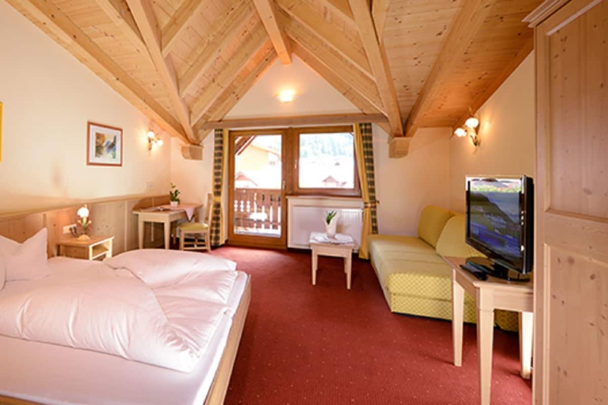 A hotel room with a large bed, a television, a desk, and a window with a view of the outside.