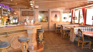 Una zona de bar con taburetes, una barra y un área de asientos con mesas y sillas.