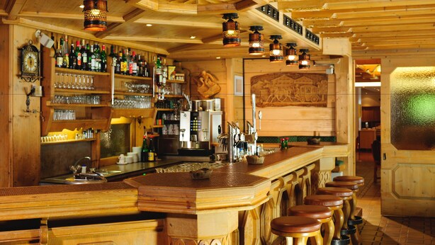 Un bar con decoración de madera, estantes con botellas, vasos y un reloj.