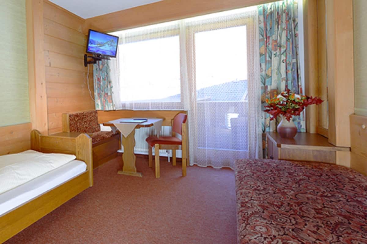 A hotel room with a bed, a desk, a chair, a television, and a window with curtains.