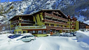 Un edificio de varios pisos con balcones, identificado con la leyenda "GASTHOF NEUE POST", rodeado de montañas cubiertas de nieve.