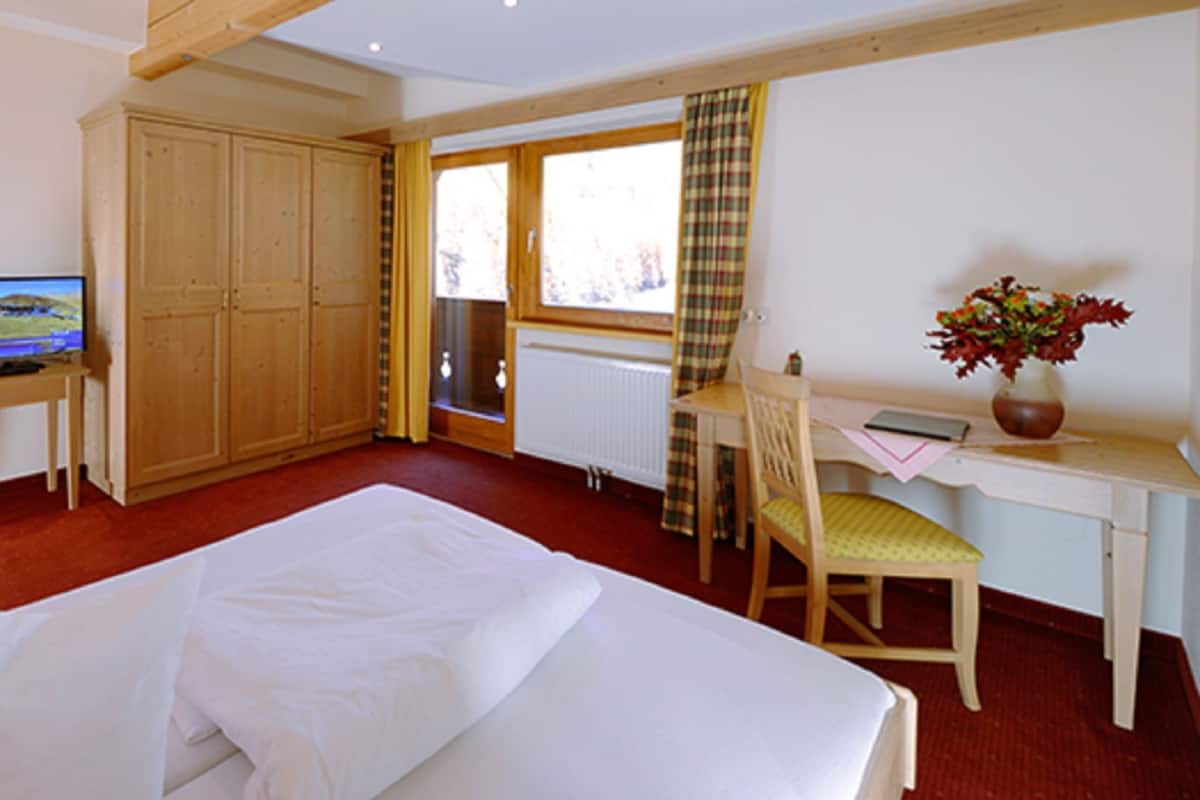 A hotel room with a bed, a desk with a chair, a television, and a window with curtains.