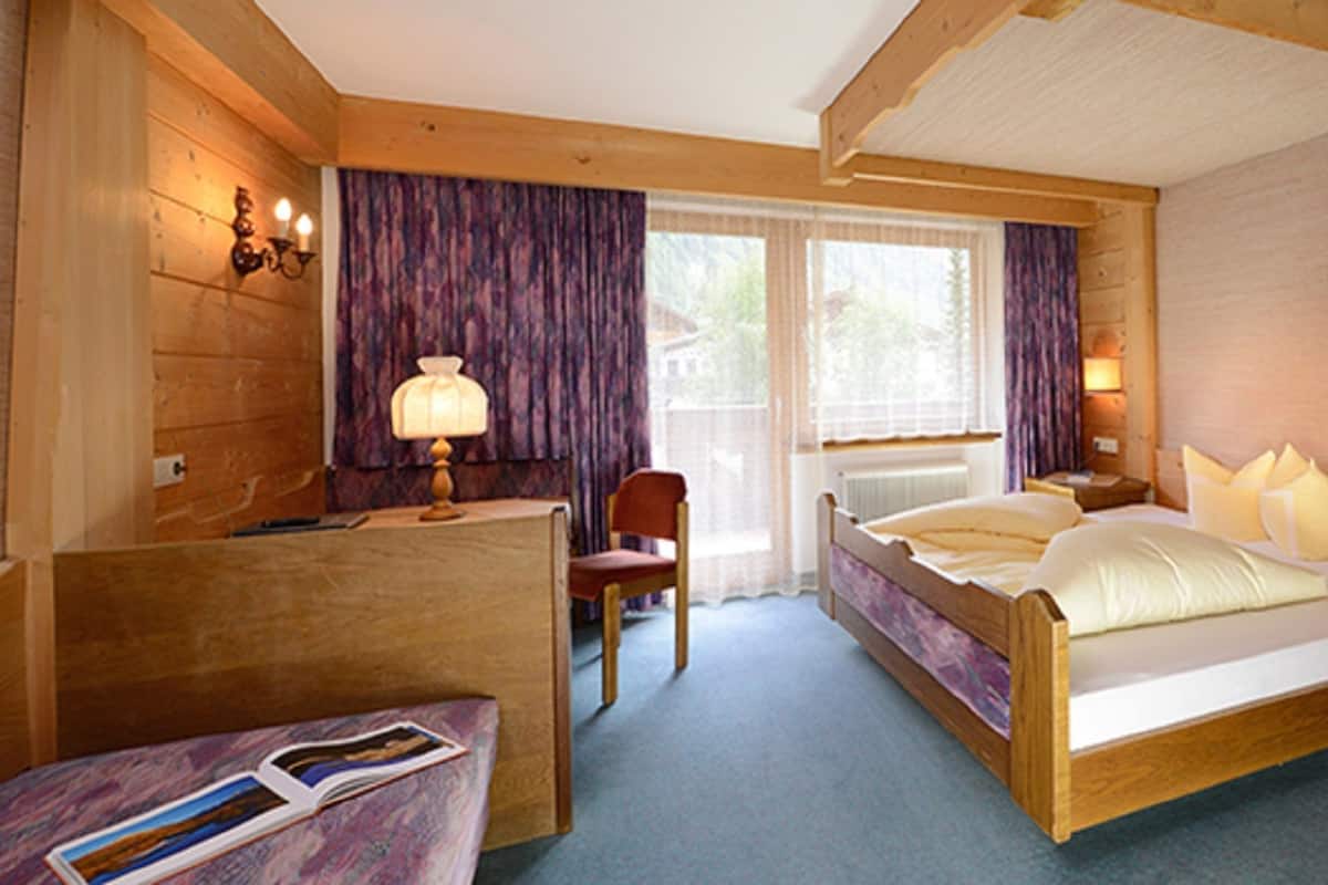 A wooden cabin bedroom with a bed, bedside table, lamp, chair, and a small desk with a chair.