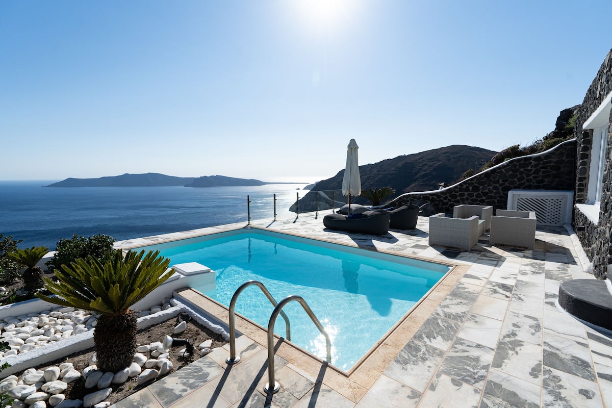 A rectangular pool with a clear blue water, surrounded by stone tiles, white rocks, and a few potted plants.