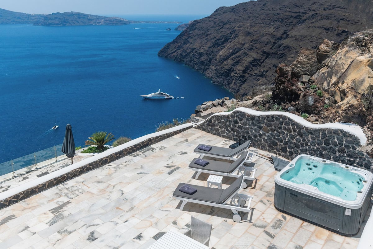 A terrace with a view of the sea, stone walls, and a hot tub.