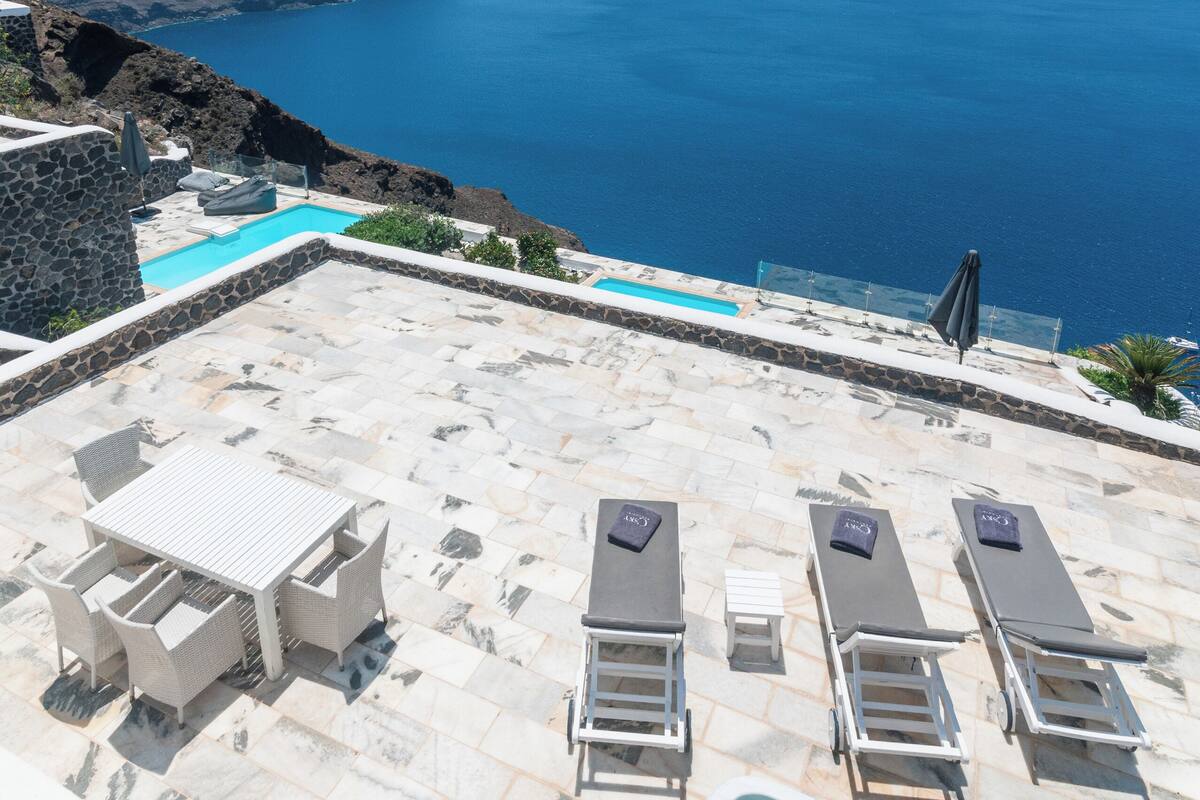 A pool area with lounge chairs and a hot tub overlooking a scenic ocean view.