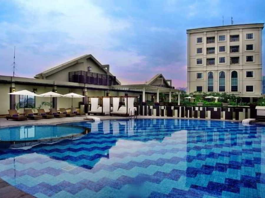 A swimming pool with a tiled deck, lounge chairs, and a building with a balcony in the background.