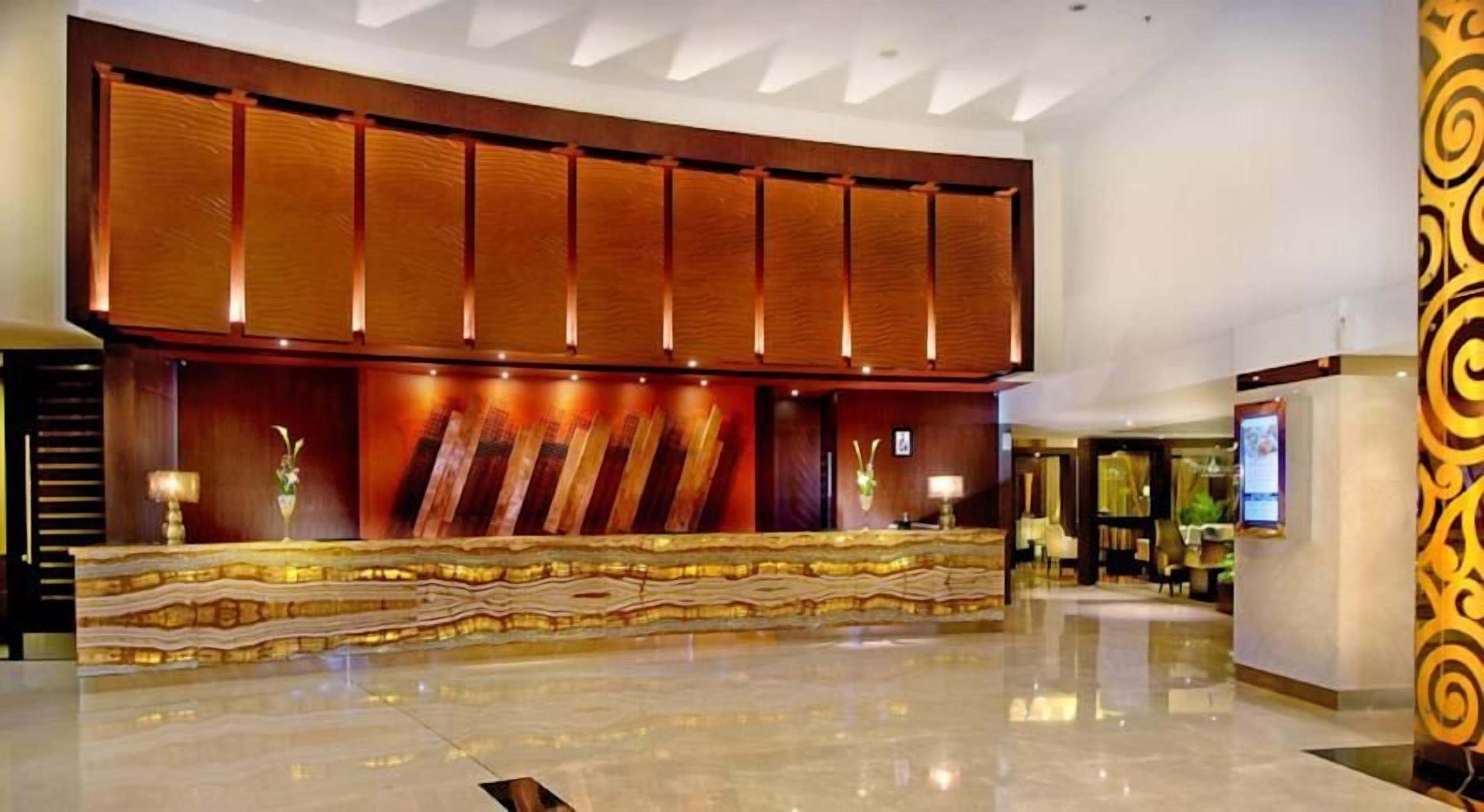 A hotel lobby with a reception desk, a large wooden panel wall, and a polished floor.