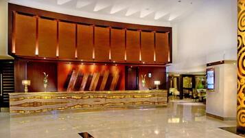 A hotel lobby with a reception desk, a large wooden panel wall, and a polished floor.