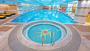 An indoor swimming pool with a sun design, surrounded by lounge chairs and a tiled floor.